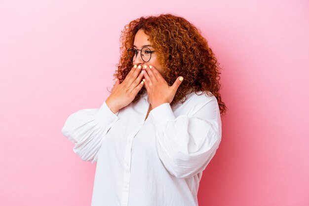 Jeune femme sinueuse latine isolée sur un mur rose en riant de quelque chose, couvrant la bouche avec les mains.