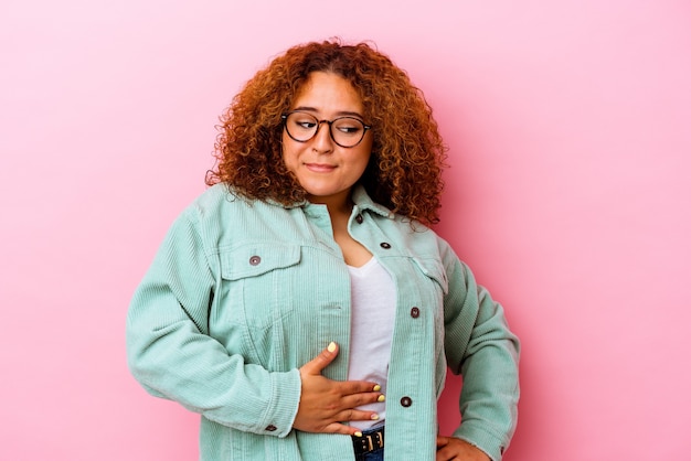 Jeune femme sinueuse latine isolée sur le mur rose touche le ventre, sourit doucement, concept de manger et de satisfaction.