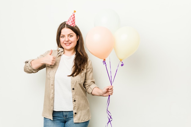 Jeune femme sinueuse de taille plus célébrant un anniversaire souriant et levant le pouce vers le haut