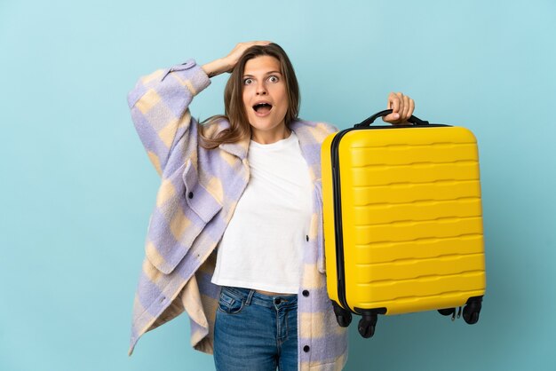 Jeune femme slovaque isolée sur fond bleu en vacances avec valise de voyage et surprise