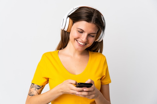 Jeune femme slovaque isolée sur un mur blanc, écouter de la musique et à la recherche de mobile