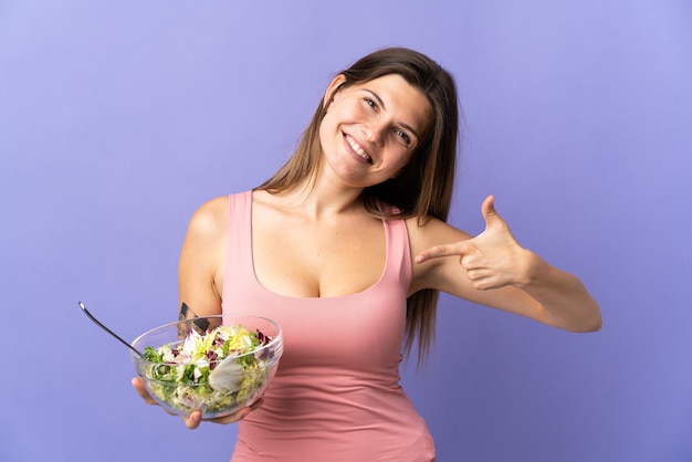 Jeune femme slovaque isolée sur mur violet avec une expression heureuse tout en pointant un bol de salade