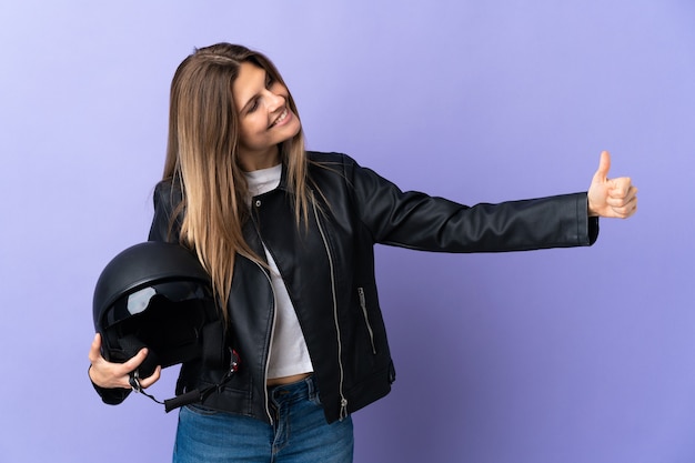 Jeune femme slovaque tenant un casque de moto isolé sur fond violet donnant un geste de pouce en l'air