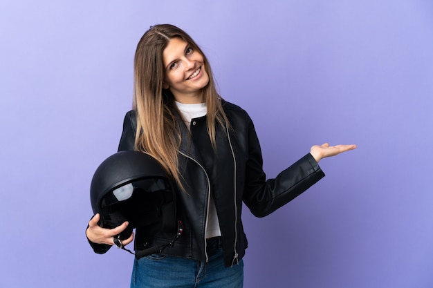 Jeune femme slovaque tenant un casque de moto isolé sur violet s'étendant les mains sur le côté pour inviter à venir