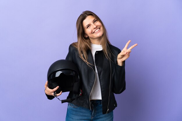 Jeune femme slovaque tenant un casque de moto isolé sur violet souriant et montrant le signe de la victoire