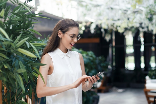 Jeune femme avec un smartphone debout dans le hall d'un restaurant confortable