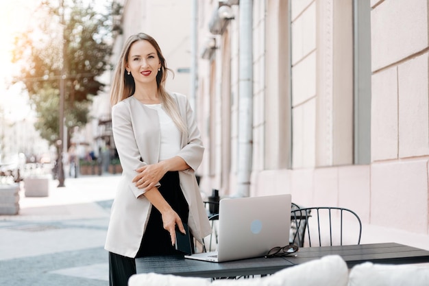 Jeune femme avec un smartphone debout près d'une table d'un café en plein air