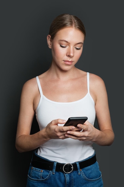 Une jeune femme avec un smartphone, une fille qui envoie des messages sur un fond gris.