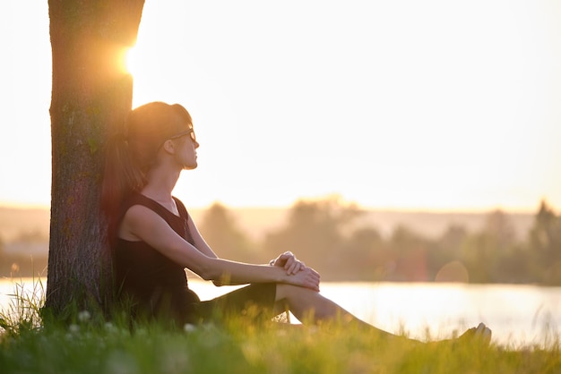 Jeune femme solitaire assise seule sur la pelouse au bord du lac profitant d'une soirée chaude Bien-être et détente dans le concept de la nature