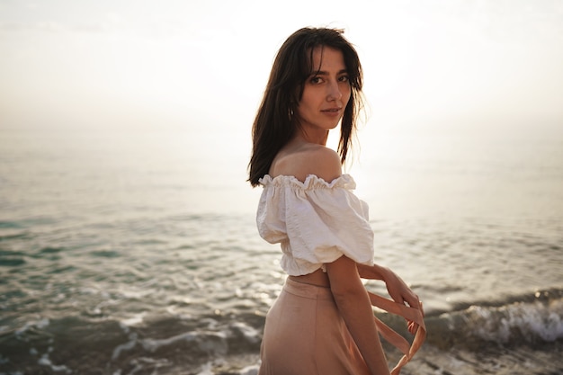 Jeune femme solitaire marche sur le bord de mer au coucher du soleil