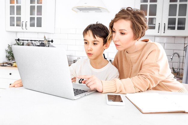 Photo une jeune femme et son fils sont assis à la table près de l'ordinateur portable et font leurs devoirs.