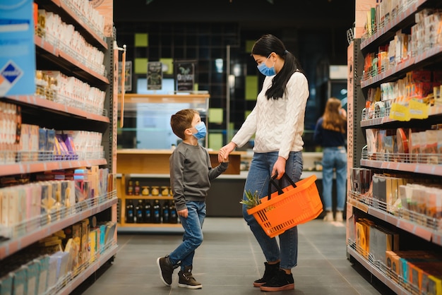 Jeune femme et son petit fils portant un masque protecteur acheter un aliment dans un supermarché