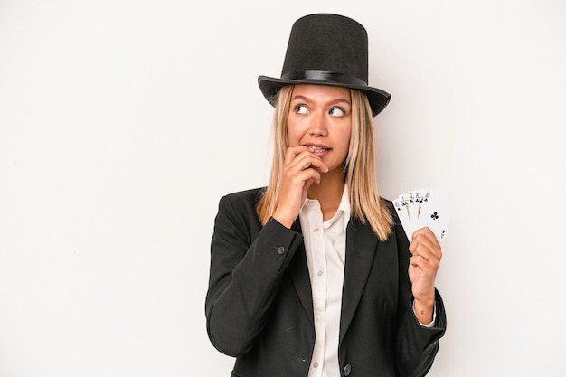 Jeune femme de sorcier caucasien tenant une carte magique isolée sur fond blanc détendue en pensant à quelque chose en regardant un espace de copie.