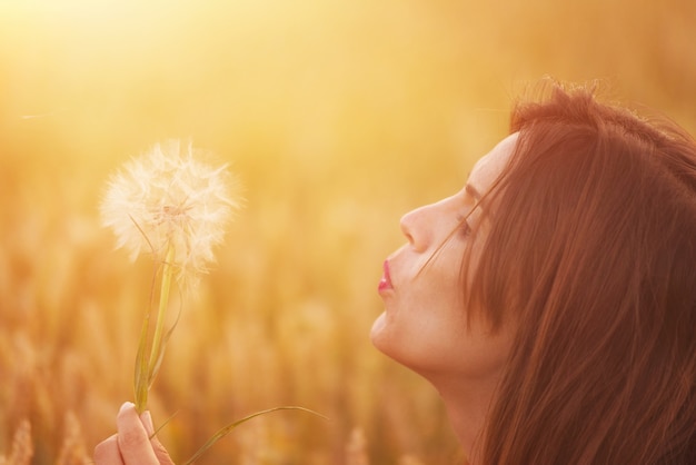 Jeune femme soufflant pissenlit dans le paysage d&#39;automne au coucher du soleil