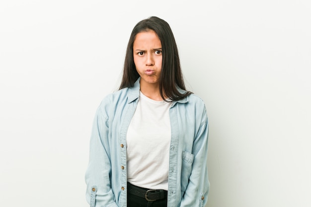 Jeune femme souffle les joues, a une expression fatiguée