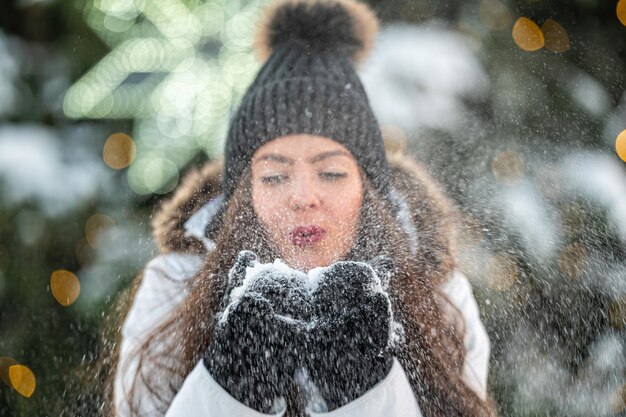 La jeune femme souffle la neige de ses mains tout en se tenant sur le fond d'un arbre de Noël