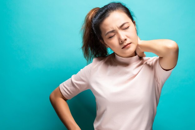 Une jeune femme souffrant de maux de cou sur un fond turquoise
