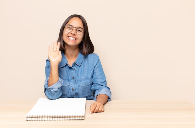 Jeune femme souriant joyeusement et gaiement, agitant la main, vous accueillant et vous saluant, ou vous disant au revoir