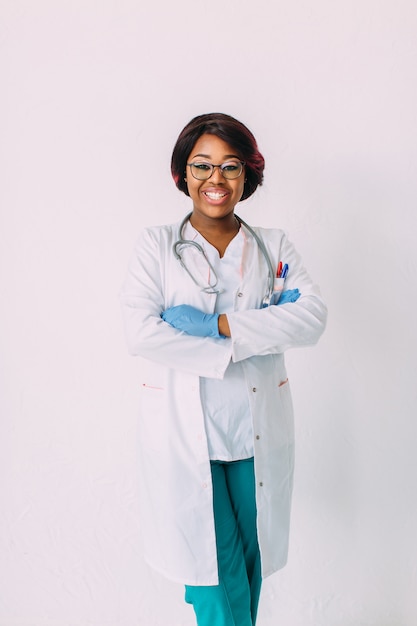 Jeune femme souriante afro-américaine médecin en gants et vêtements médicaux, isolé sur blanc