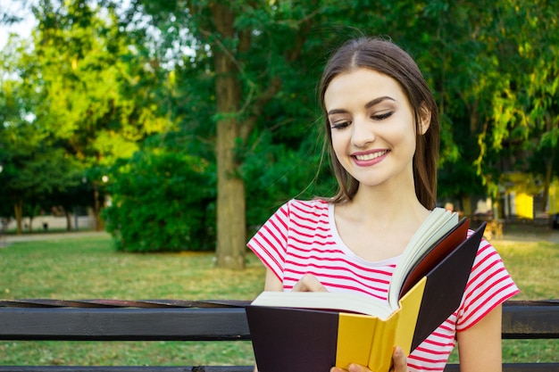 Jeune femme souriante assise avec journal prenant des notes dans le magnifique parc de la ville