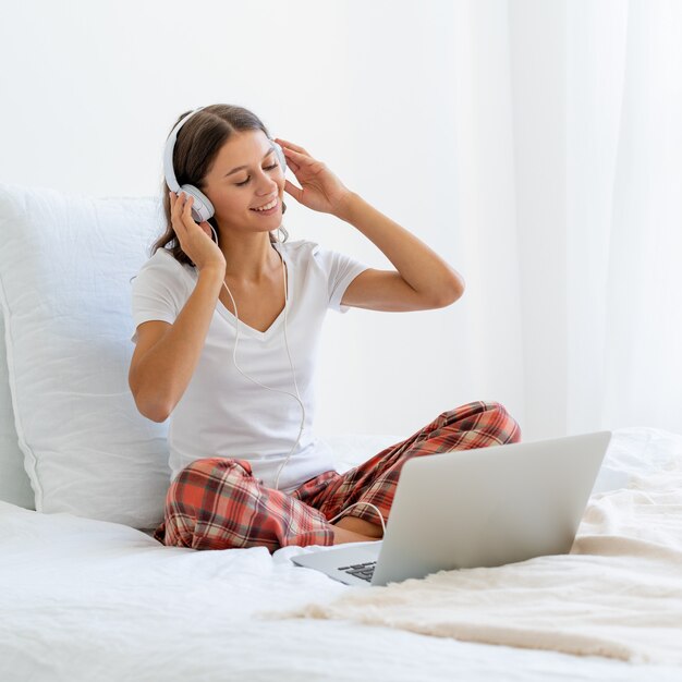 Jeune femme souriante assise sur le lit dans la chambre et écouter de la musique ou regarder un film