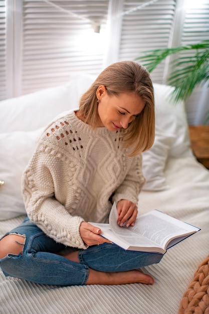 Jeune femme souriante assise sur le lit avec un livre