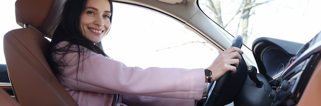 Jeune femme souriante au volant d'une voiture de luxe en gros plan