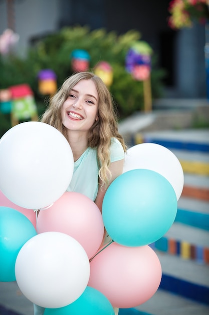 Jeune femme souriante avec des ballons multicolores volants dans la ville