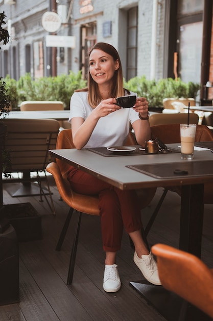 Jeune femme souriante boit du café dans un café de la rue