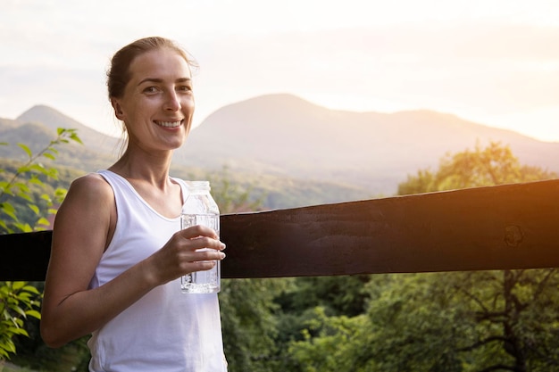 Jeune femme souriante avec une bouteille d'eau profitant d'un paysage naturel avec vue sur la montagne