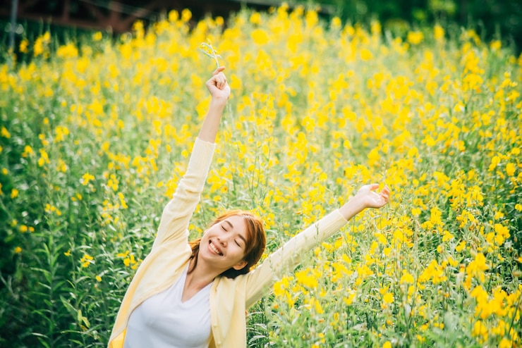 Photo une jeune femme souriante avec les bras levés debout contre des plantes à fleurs jaunes