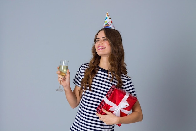 Jeune femme souriante en casquette de célébration tenant un cadeau rouge et une coupe de champagne