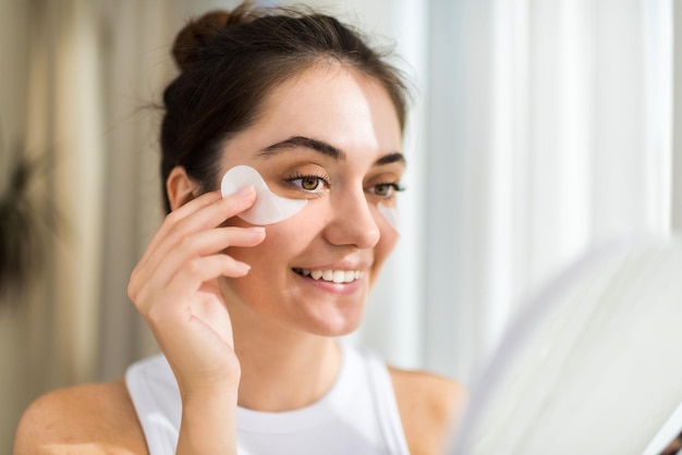 Une jeune femme souriante caucasienne avec des taches sous les yeux regardant dans le miroir Thème des soins de la peau