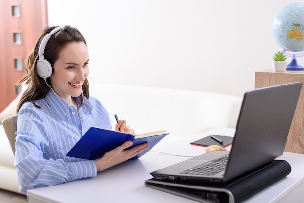 Jeune femme souriante en chemise bleue avec un casque assis à un ordinateur portable