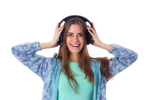 Jeune femme souriante en chemise bleue écoutant de la musique dans des écouteurs noirs en studio