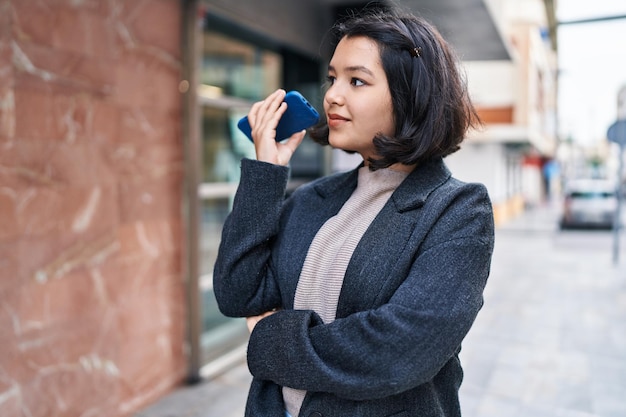 Jeune femme souriante et confiante écoutant un message audio par le smartphone dans la rue