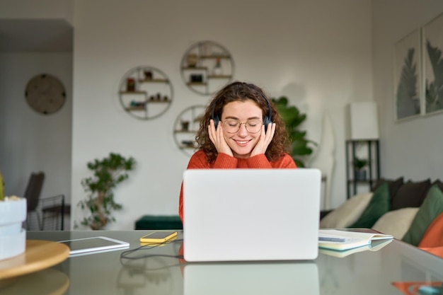 Jeune femme souriante dans des écouteurs écoutant de la musique de podcast apprendre à la maison