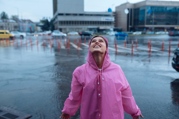 Jeune femme souriante dans un imperméable rose profitant d'un jour de pluie