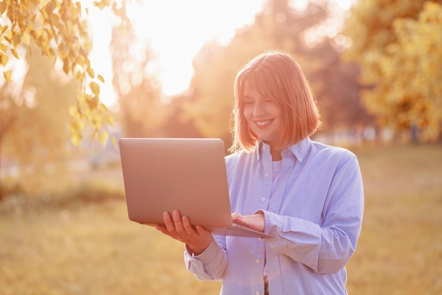 Jeune femme souriante dans un parc verdoyant avec ordinateur portable