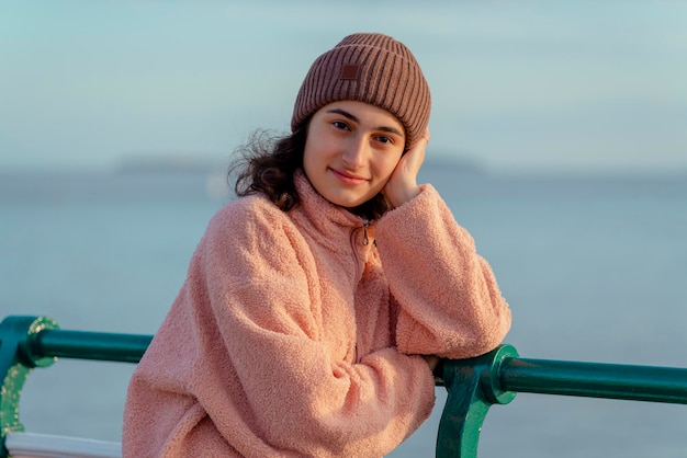 Une jeune femme souriante debout sur la jetée en regardant la mer au coucher du soleil