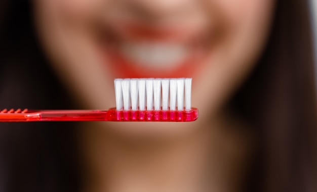 Une jeune femme souriante avec des dents saines tient une brosse à dents. Mise au point sélective. Photo recadrée. Arrière-plan flou.