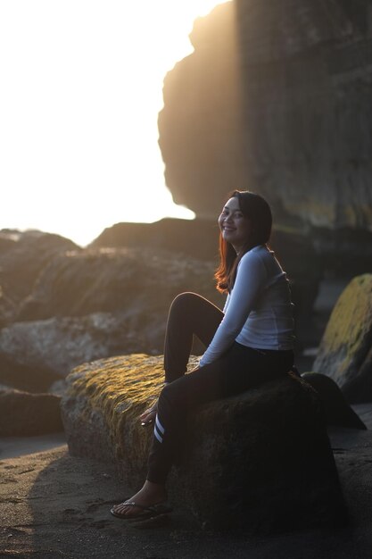 Photo une jeune femme souriante détournant le regard alors qu'elle est assise sur un rocher.