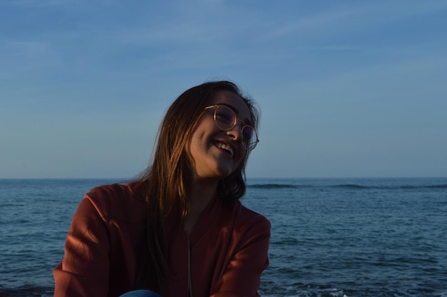 Une jeune femme souriante détournant son regard vers la mer.