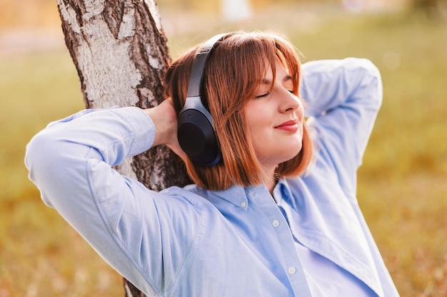 Jeune femme souriante écoutant de la musique avec un casque au coucher du soleil fille casque noir sans fil