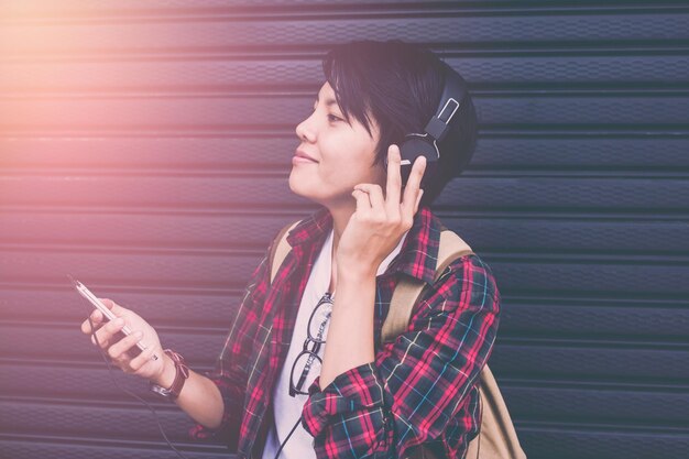 Une jeune femme souriante écoute de la musique sur des écouteurs alors qu'elle se tient contre l'obturateur