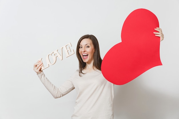 Jeune femme souriante efficace tenant un grand coeur rouge, amour de mot en bois sur fond blanc. Copiez l'espace pour la publicité. Avec place pour le texte. Concept de la Saint-Valentin ou de la Journée internationale de la femme.