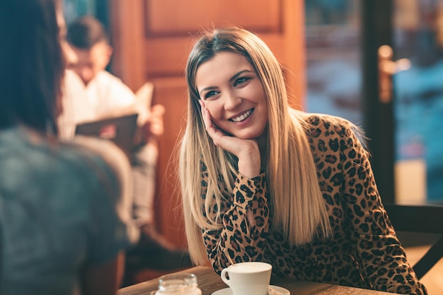 Une jeune femme souriante est assise avec sa chère amie dans le café, buvant du café.