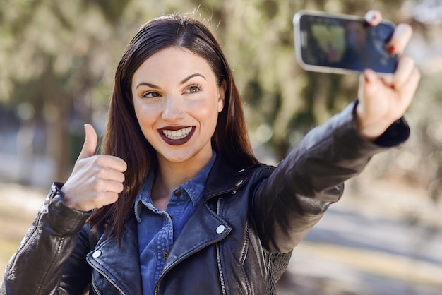 Photo une jeune femme souriante fait des gestes avec le pouce en l'air tout en prenant un selfie dans le parc.