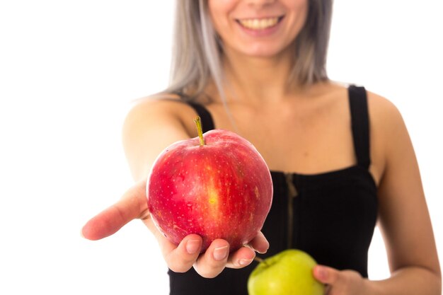 Jeune femme souriante en haut noir montrant une pomme rouge sur fond blanc en studio