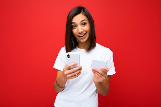 Jeune femme souriante et heureuse portant des vêtements de tous les jours isolés sur fond tenant un téléphone et